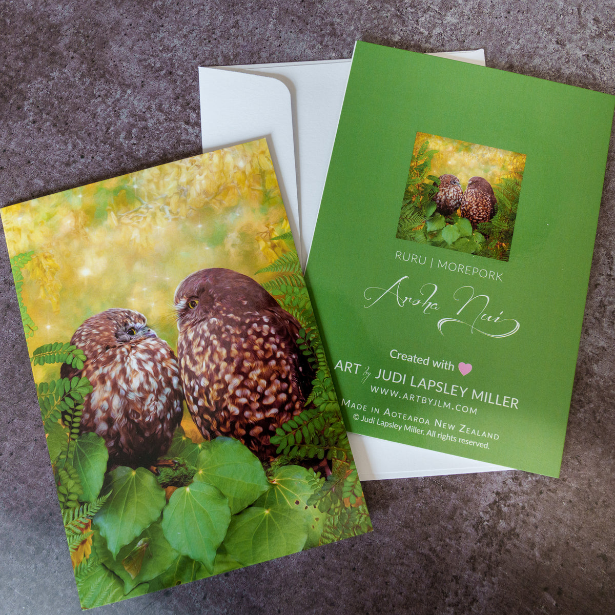 Greeting cards and envelope featuring two morepork ruru owls staring at each other amidst flowering kowhai and native leaves.