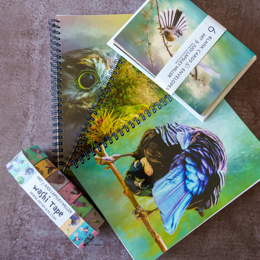 A bird-themed stationery set arranged on a textured brown surface, including 3 spiral bound notebooks, a wrapped card set labeled '6 cards & envelopes', and a wrapped tape roll labeled 'washi tape'.