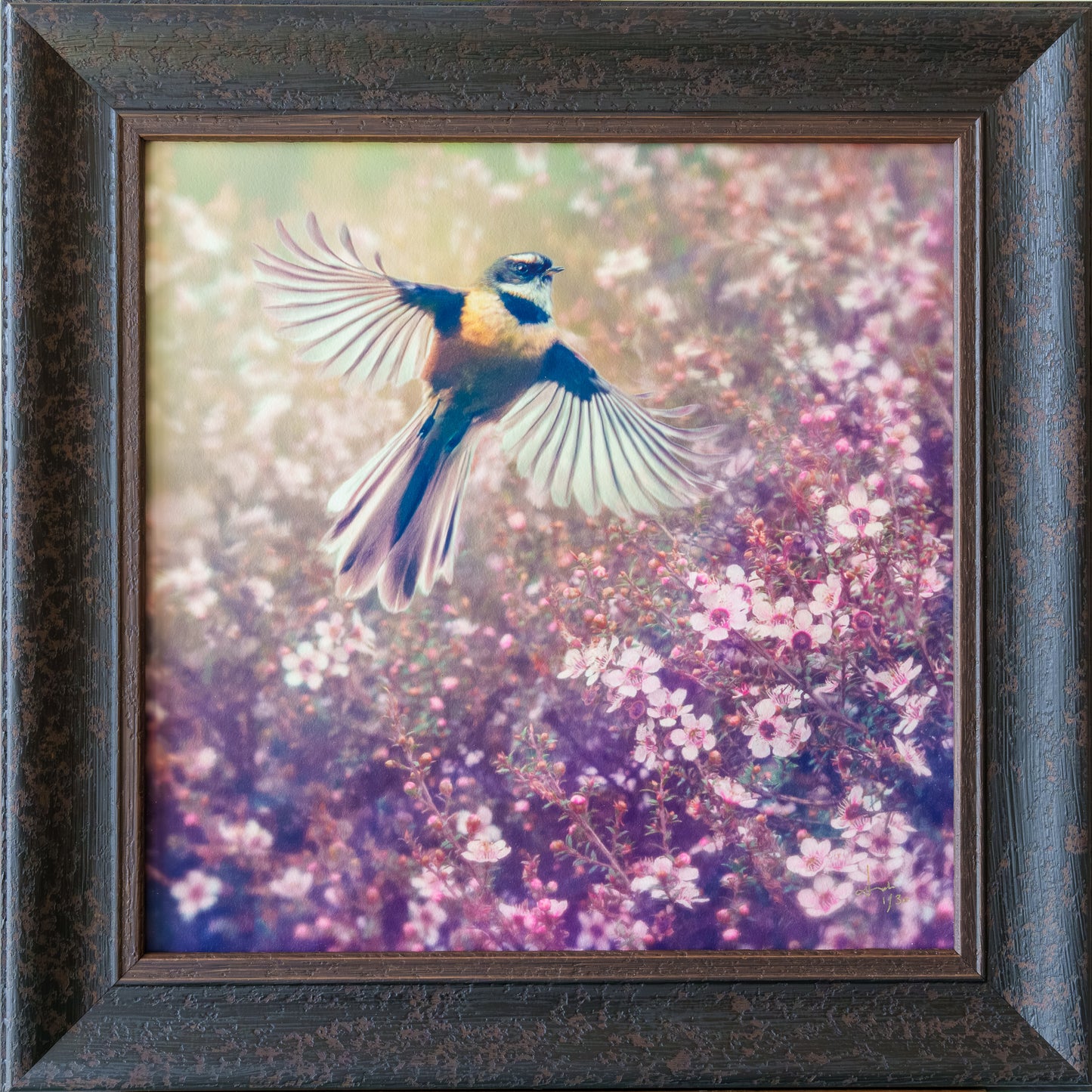 Framed square wall art featuring a small bird in flight over pink and purple flowering plants, set in a dark textured wooden frame.