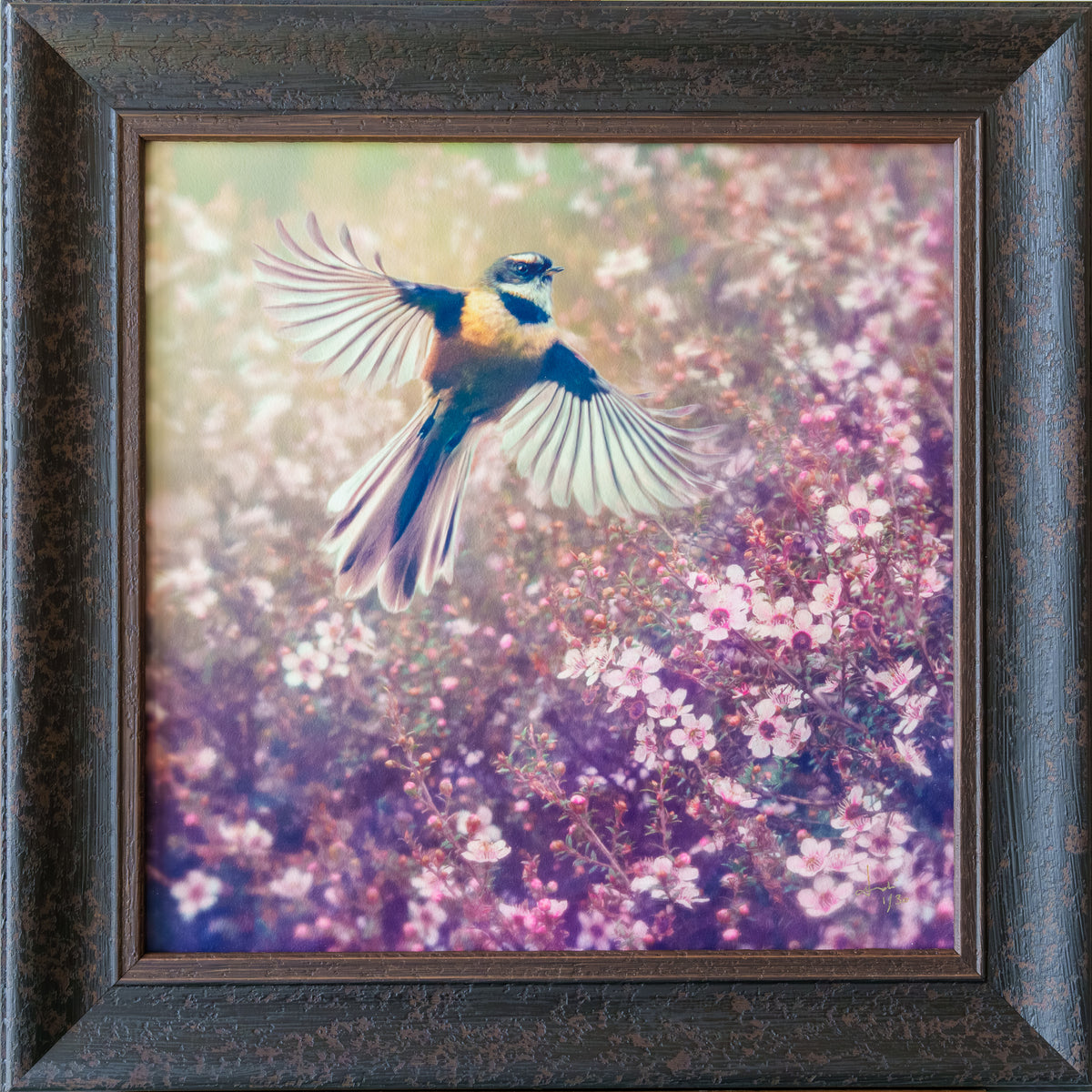 Framed square wall art featuring a small bird in flight over pink and purple flowering plants, set in a dark textured wooden frame.