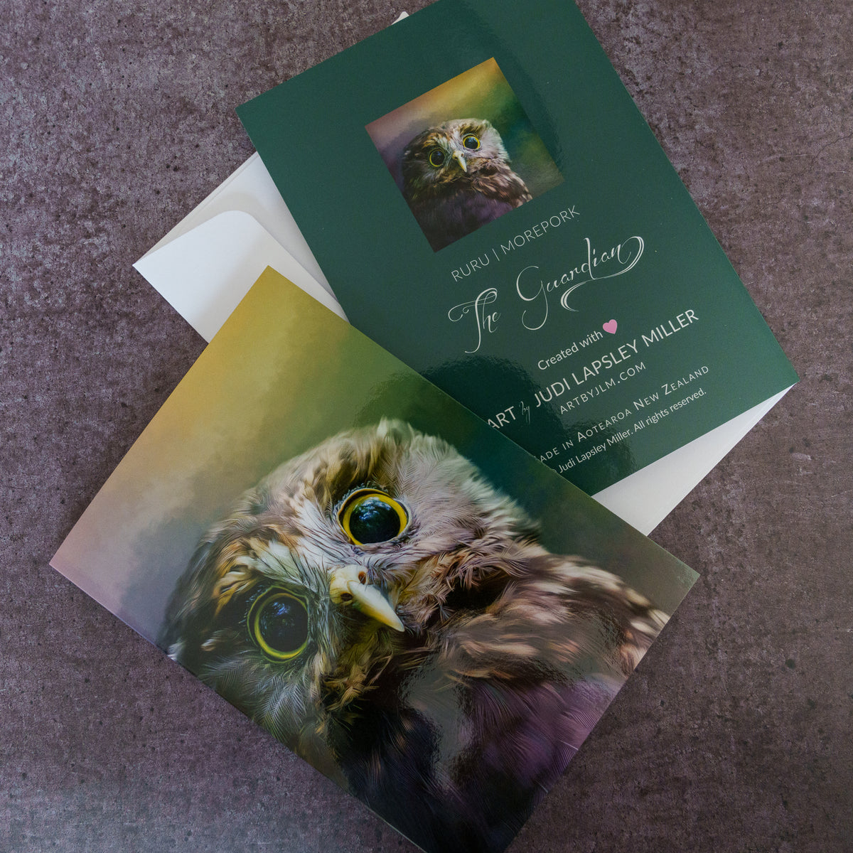 Two printed owl-themed cards laid on a textured gray surface, with one dark green card showing owl photography and text, and another owl portrait card partially covering it.
