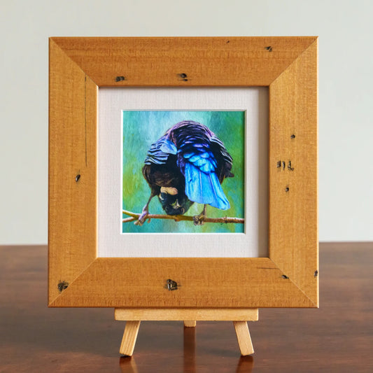 Framed painting of a colorful bird on a branch with a wooden frame and easel.