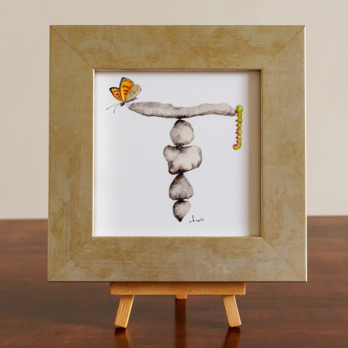 Framed artwork of stacked stones with a butterfly and caterpillar on a white background
