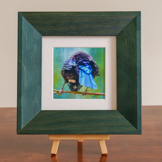 Framed painting of a bird on a branch with a green frame and wooden easel.