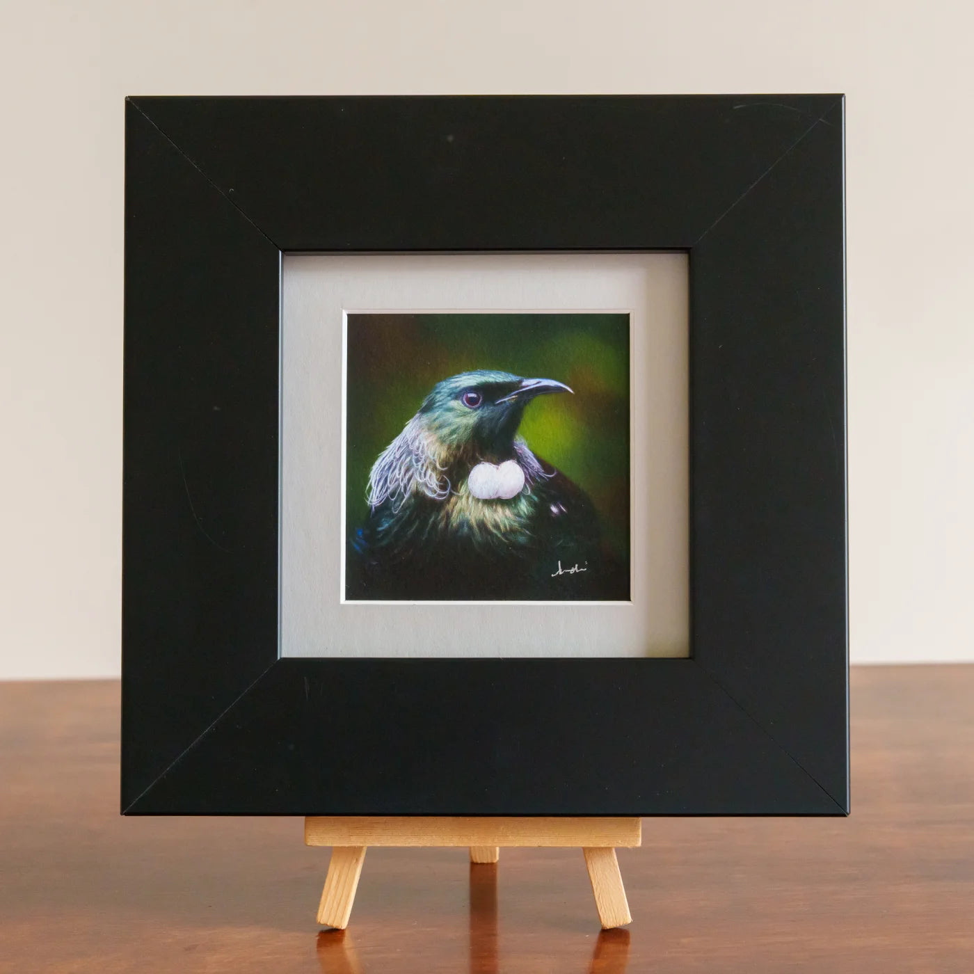 Framed painting of a bird on a wooden easel against a plain background