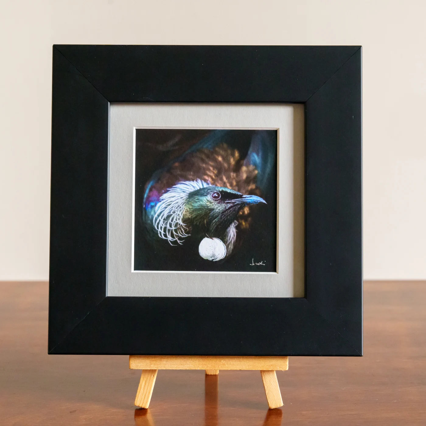 Framed artwork of a colorful bird on a wooden easel against a beige background