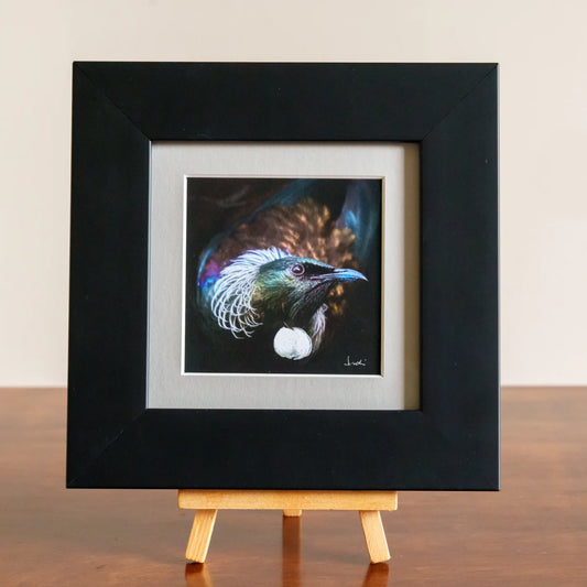 Framed artwork of a colorful bird on a wooden easel against a beige background