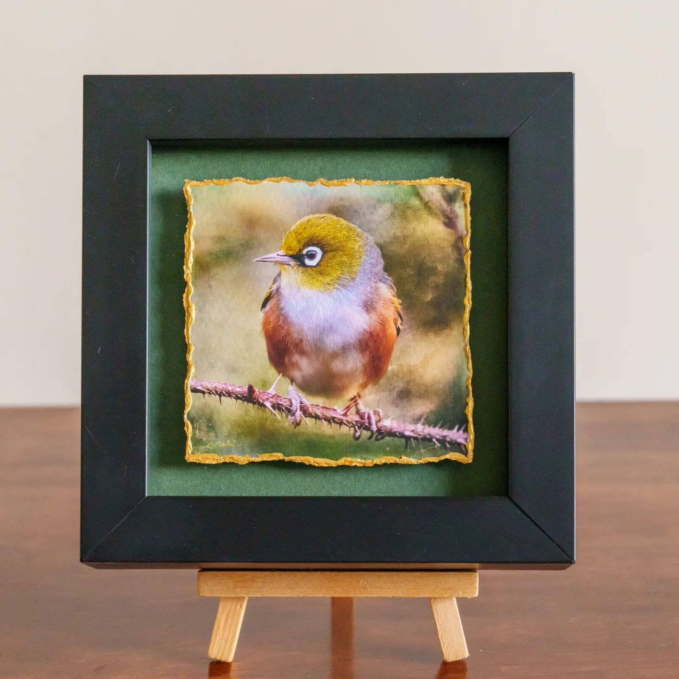 Framed artwork of a bird on a branch with a black frame and green mat.