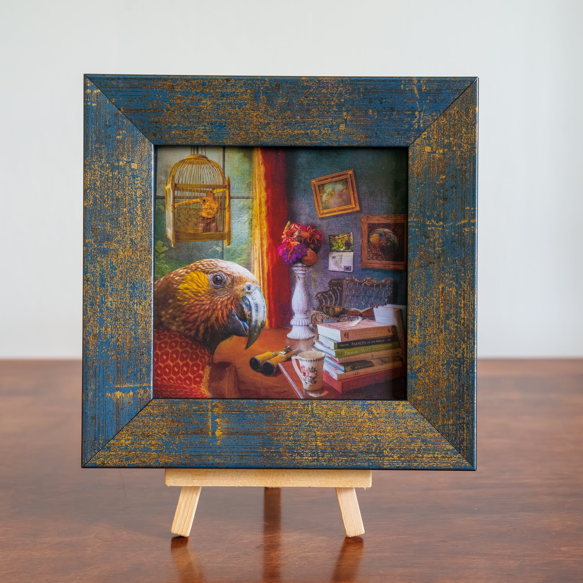 Framed artwork of a parrot in a room with books and a birdcage.