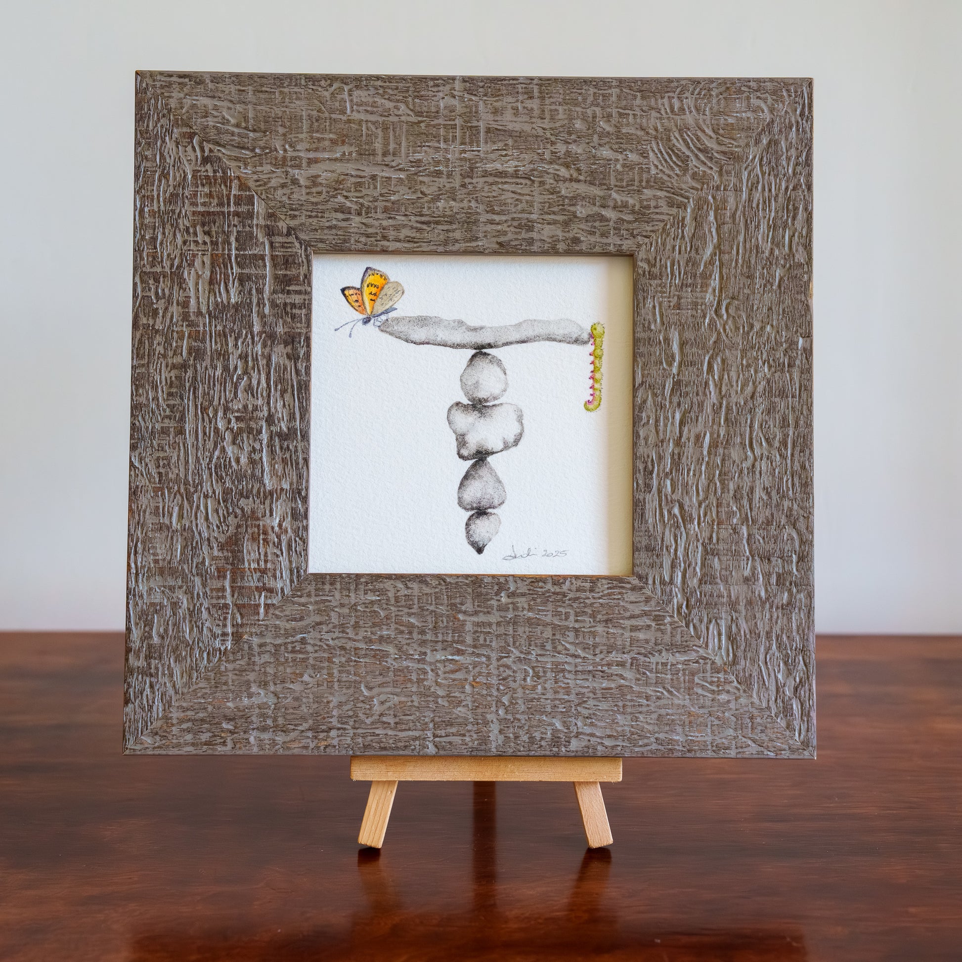 Framed artwork of a butterfly and stacked stones on a small easel