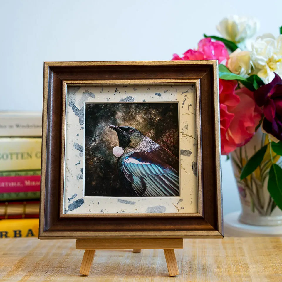 A print of a tui framed as a TinyArt piece. The frame is brown and gold and the mat is covered with a blue leaf washi paper.